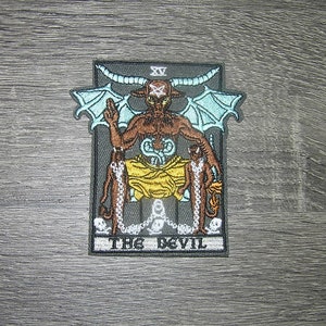 May include: Embroidered patch featuring a detailed illustration of The Devil tarot card. The design includes a horned figure with wings, chains, and the text "THE DEVIL" at the bottom. The patch has a gray border and is set against a wooden background.