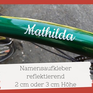 May include: A green bicycle frame with the name "Mathilda" in white script. The image also shows a white sticker with German text: "Namensaufkleber reflektierend 2 cm oder 3 cm Höhe."