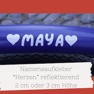 Könnte beinhalten: Ein blauer Fahrradrahmen mit dem Namen "MAYA" in Weiß, flankiert von weißen Herzformen. Das Bild zeigt auch Text: "Namensaufkleber 'Herzen' reflektierend 2 cm oder 3 cm Höhe."