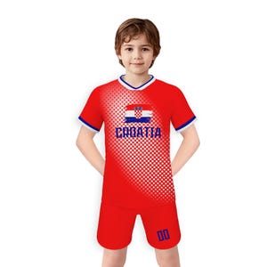 May include: A red soccer uniform with white and blue trim. The shirt features the Croatian flag and the word "CROATIA" in white. The shorts have the number "00" in blue. The uniform is worn by a young person.