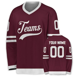 May include: Maroon hockey jersey with white accents. The jersey features the word "Teams" in a script font on the front. The back of the jersey has the text "YOUR NAME" above the number "00". White stripes adorn the sleeves.