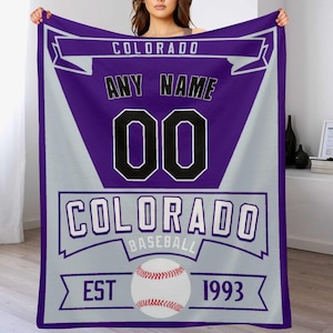 May include: Purple and gray baseball themed fleece blanket with the text "COLORADO" and "ANY NAME 00 COLORADO BASEBALL EST 1993". A baseball is featured in the center of the blanket.