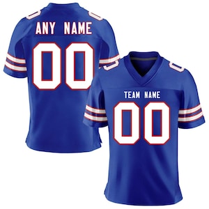 Op de afbeelding: Twee blauwe voetbalshirts. Eén shirt heeft "ANY NAME" boven het nummer "00" op de rug. De andere heeft "TEAM NAME" boven het nummer "00" op de voorkant. Beide shirts hebben witte en rode accenten.