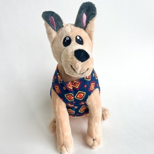 May include: A plush toy dog with brown fur, gray ears, and big black eyes. The dog is wearing a blue and orange patterned shirt.