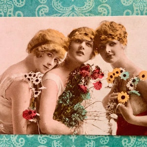 May include: Three women with blonde hair and flowers in their hair. The women are wearing white dresses and are holding bouquets of flowers. The image is in a vintage style.