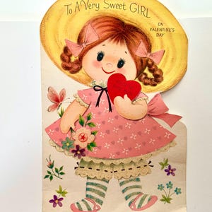 May include: A vintage Valentine's Day card featuring a cartoon girl wearing a straw hat and holding a red heart. The card reads "To A Very Sweet Girl On Valentine's Day."