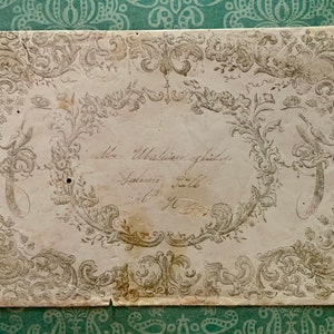 May include: An antique, off-white paper with a decorative border of intricate floral designs and a bird. The paper has a handwritten inscription that reads "Mrs. Whittington's address, Johnsonville, South Carolina."