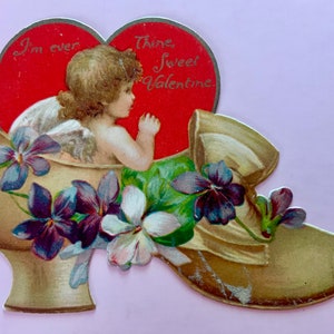 Tarjeta vintage del Día de San Valentín Cupido sentado dentro de un zapato lleno de violetas Nister