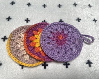 Peut inclure: Trois torchons en crochet de couleur violette, orange et jaune. Les torchons sont empilés les uns sur les autres.