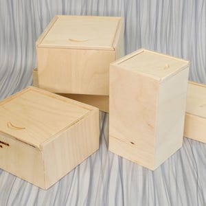 Puede incluir: Cuatro cajas de madera con tapas, apiladas y dispuestas sobre una superficie texturizada gris claro. Las cajas son de madera clara y tienen un diseño simple y minimalista. La caja superior tiene el texto "Air Compressor Accessories" grabado en la parte delantera.