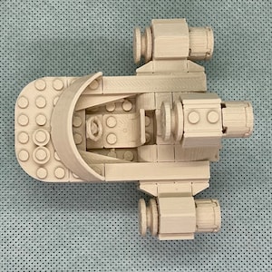 May include: A white Lego spaceship model with a cockpit and two engines. The model is made of Lego bricks and is designed to look like a futuristic spacecraft.