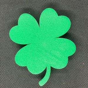 May include: A green four-leaf clover cutout, a symbol of good luck, is displayed against a black background.