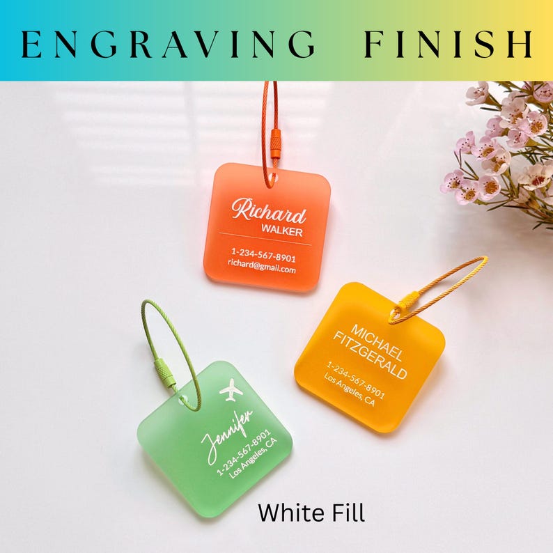 May include: Three personalized luggage tags in orange, yellow, and green. Each tag has a different name and contact information in white. The tags are square with rounded corners and have a loop for attachment. The text "ENGRAVING FINISH" and "White Fill" are also visible.