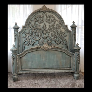May include: A large, ornate bed frame with a distressed blue-green finish. The headboard features elaborate, carved floral and scrollwork details, with silver accents. The bed frame has four posts and a footboard, all with matching decorative elements.