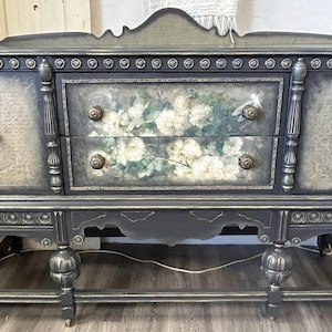 May include: A black painted vintage buffet with two drawers and two doors. The drawers have a floral design and the doors have a decorative pattern. The buffet has turned legs and a gold trim.