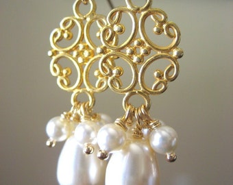 Peut inclure: Boucles d'oreilles en filigrane dorées avec des fausses perles pendantes. Les boucles d'oreilles présentent un motif ajouré orné avec un groupe de petites perles et une plus grande perle en forme de goutte. Les boucles d'oreilles sont suspendues à des crochets d'oreilles dorés.