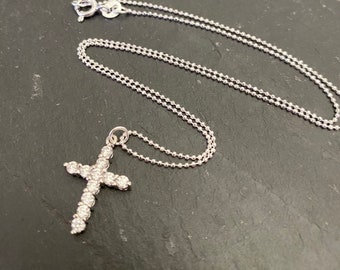 May include: A silver chain necklace with a small, sparkling cross pendant. The cross is made of silver and is covered in small, clear stones.