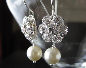 Könnte beinhalten: Elegante silberne Ohrringe mit einem floralen Design, das mit klaren Kristallen besetzt ist. Jeder Ohrring hat eine herabhängende cremefarbene Perle, die einen raffinierten und zeitlosen Look erzeugt. Die Ohrringe sind an einem silbernen Haken aufgehängt.