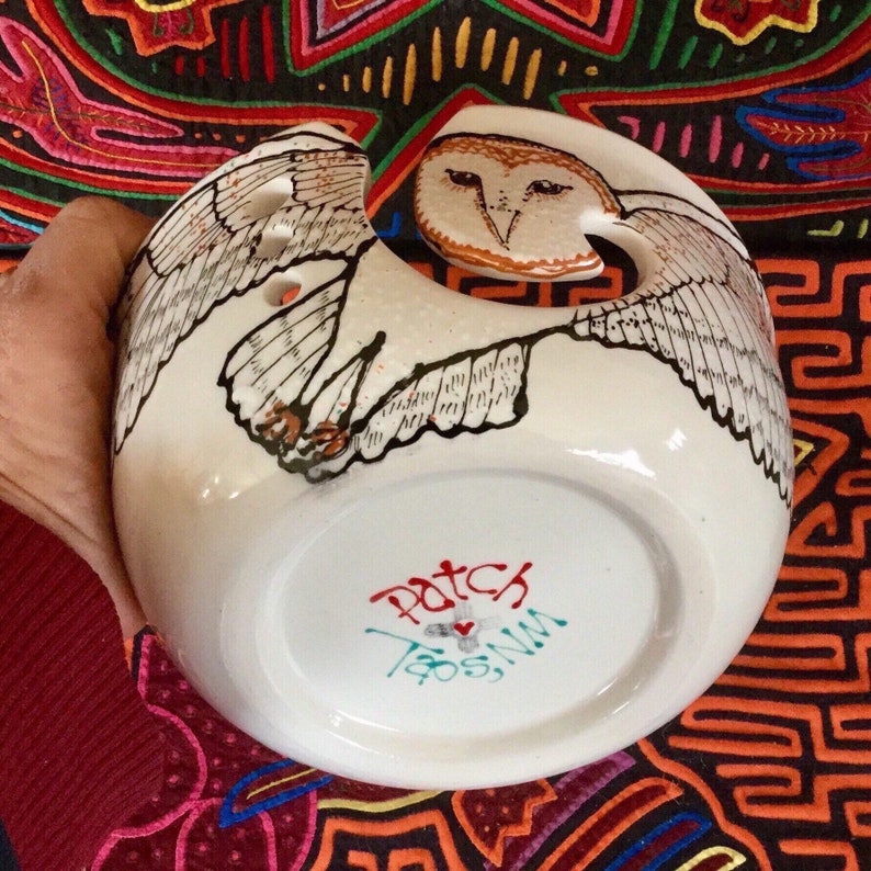 Op de afbeelding: Witte keramische garenkom met een handgeschilderd schuuruil-ontwerp. De uil heeft bruine ogen en een lichtbruine snavel. De kom heeft drie gaten voor garen. De bodem van de kom is gesigneerd met "Patch Taos, NM".