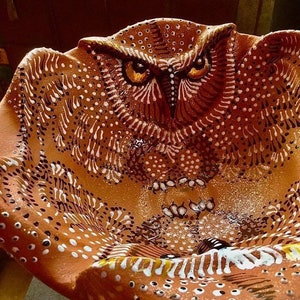 May include: A terracotta owl-shaped bowl with white and brown painted details. The owl's eyes are painted with yellow and black accents. The bowl is decorated with a pattern of dots and lines.