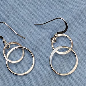 May include: A pair of silver earrings featuring two interlocking circles. The earrings have a simple, modern design.