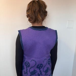 Pu&ograve; includere: Gilet di maglia viola con bordatura blu e un motivo di teschi neri e fiori sul fondo.
