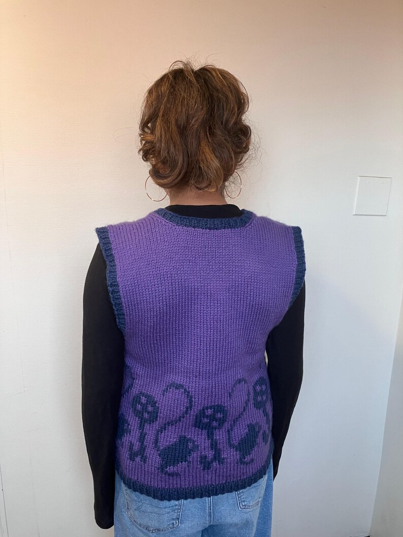 Pu&ograve; includere: Gilet di maglia viola con bordatura blu e un motivo di teschi neri e fiori sul fondo.
