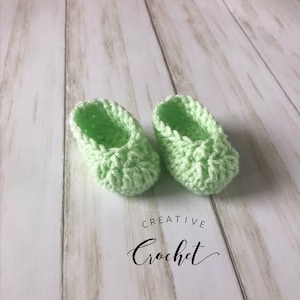 May include: A pair of light green crocheted baby booties. The booties are made with a textured stitch and have a simple, classic design.