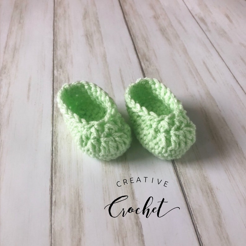 May include: A pair of light green crocheted baby booties. The booties are made with a textured stitch and have a simple, classic design.