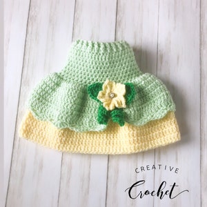 May include: A green and yellow crocheted baby hat with a flower embellishment. The hat is made with a soft yarn and has a delicate design.  The flower is made with green and yellow yarn and has a small, sparkly button in the center.  The hat is perfect for a baby girl.