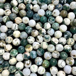 May include: A collection of round, polished moss agate gemstones. The stones vary in color, with shades of white, green, and brown. The gemstones are smooth and have unique patterns, creating a natural and earthy aesthetic.