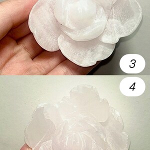 May include: Two views of a carved, light pink rose. The stone flower has detailed petals and a textured surface. The rose is held in a hand, with the numbers 3 and 4 visible in the background.