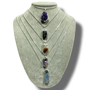 May include: Five silver necklaces with different crystal pendants. The pendants are amethyst, black tourmaline, citrine, amethyst, and blue kyanite.