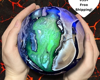 May include: A decorative, spherical object with a blue, green, and white design, resembling a stylized Earth. The object is held in two hands against a background of red and black patterns. The object has a glossy finish.