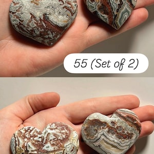 May include: Two heart-shaped stones with a marbled pattern in shades of brown, white, and gray. The stones are held in a hand. The text "55 (Set of 2)" and "56 (Set of 2)" is visible.