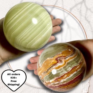May include: Two decorative onyx spheres. One is a light green color with white veining, and the other is a mix of brown, red, and green with white veining. The spheres are held in hands, showcasing their natural patterns and textures.
