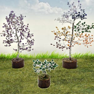 May include: Three wire wrapped crystal trees in different colors. The trees are in brown pots and are sitting on a green grassy surface.