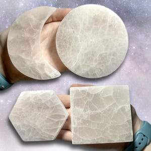 May include: Four light pink crystal shapes: a crescent moon, a circle, a hexagon, and a square. The shapes have a translucent, textured appearance. The background is a soft purple and white gradient.