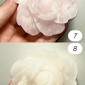 May include: Two carved rose-shaped gemstones. The top rose is a light pink color, while the bottom rose is a creamy white. The petals are detailed with carved lines. The gemstones are likely used for decorative purposes.