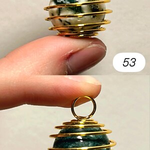 May include: Two gemstone pendants. The top pendant has a white and green stone encased in a gold-colored wire cage. The bottom pendant has a dark green stone in a similar cage. Both have a small gold loop at the top.