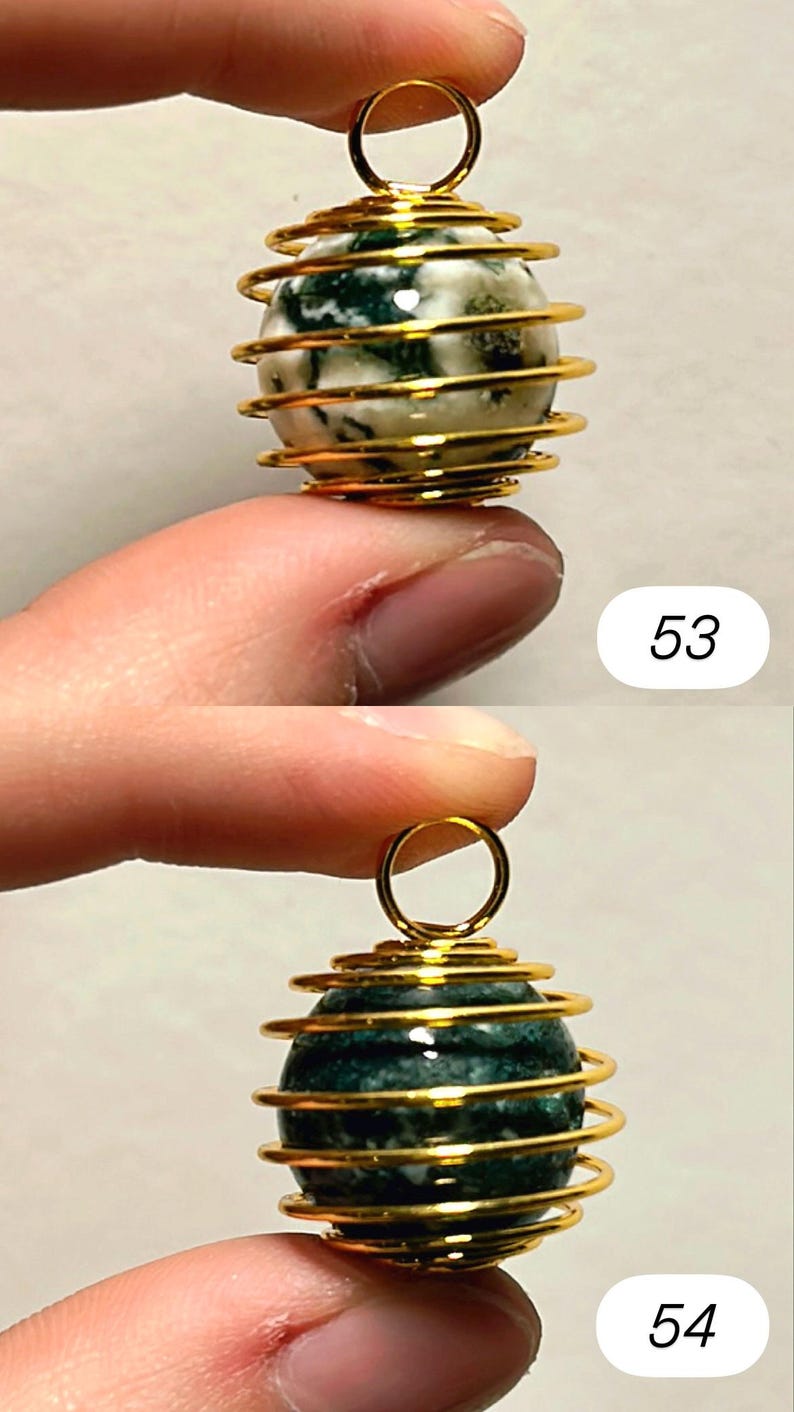 May include: Two gemstone pendants. The top pendant has a white and green stone encased in a gold-colored wire cage. The bottom pendant has a dark green stone in a similar cage. Both have a small gold loop at the top.