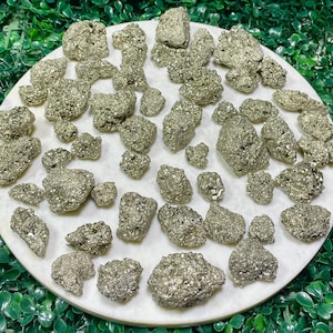May include: A collection of raw pyrite crystals, also known as fool's gold, in various sizes and shapes. The crystals are a metallic gold color with a slightly iridescent sheen. They are arranged on a white background.