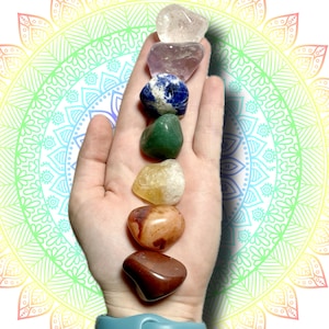 May include: A hand holds seven polished gemstones in a vertical row. The stones are various colors, including clear, purple, blue, green, yellow, orange, and brown. The background features a colorful mandala design.