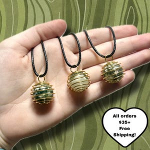 May include: Three gemstone necklaces with black cords. Each necklace features a wire-wrapped sphere pendant in gold. The spheres are made of white and green stones. The image includes text that says "All orders $35+ Free Shipping!"