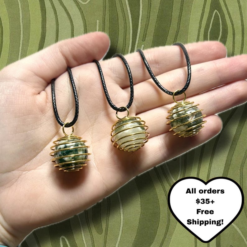 May include: Three gemstone necklaces with black cords. Each necklace features a wire-wrapped sphere pendant in gold. The spheres are made of white and green stones. The image includes text that says "All orders $35+ Free Shipping!"