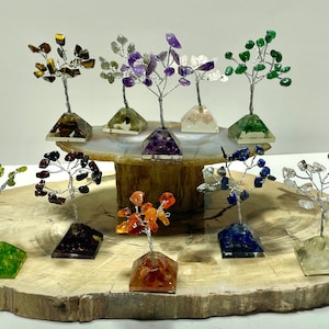 May include: A collection of 10 small crystal trees on a wooden base. The trees are made of wire and various colored crystals, including black, green, clear, purple, red, orange, and blue.
