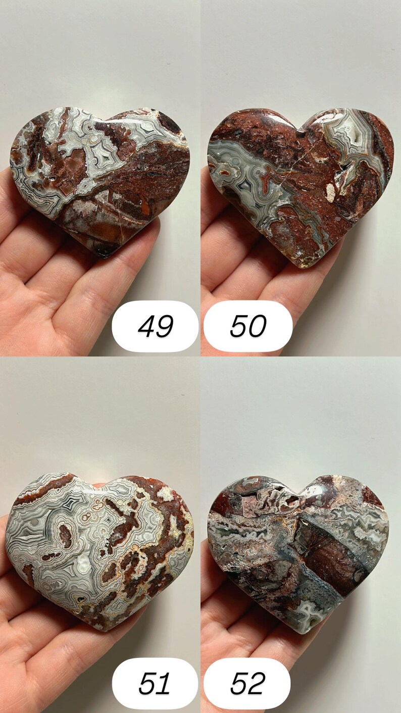 May include: Four heart-shaped stones with unique patterns and colors. The stones are held in hands and numbered 49, 50, 51, and 52. The stones have a mix of red, brown, gray, and white colors, with intricate veining and patterns throughout.