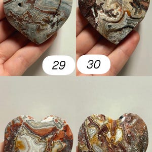 May include: Four heart-shaped stones with unique patterns and colors. The stones are held in a hand and numbered 29, 30, 31, and 32. The stones feature a mix of red, brown, gray, and white hues, with intricate veining.