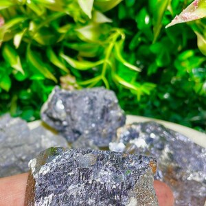 Puede incluir: Un gran cristal met&aacute;lico gris oscuro con una superficie rugosa y texturizada. El cristal tiene un brillo plateado y una forma irregular.