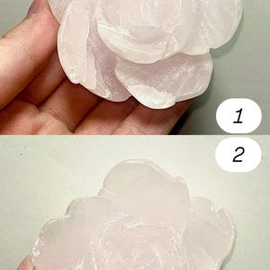 May include: A carved rose made of pale pink stone. The flower has multiple layers of petals, with a detailed texture. The rose is a light pink color and appears to be smooth. The image is taken from two different angles.